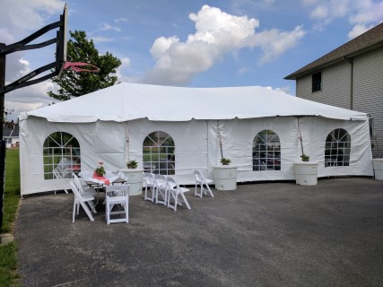 Graduation Party - 20' x 40' Frame Tent (Free Span) on Driveway, Cathedral Sidewalls, White Padded Chairs, Rectangular Tables with White Plastic Table Covers. One side anchored with Water Barrels.
